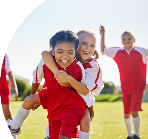 Dos niñas con uniforme de fútbol juegan y ríen en la cancha